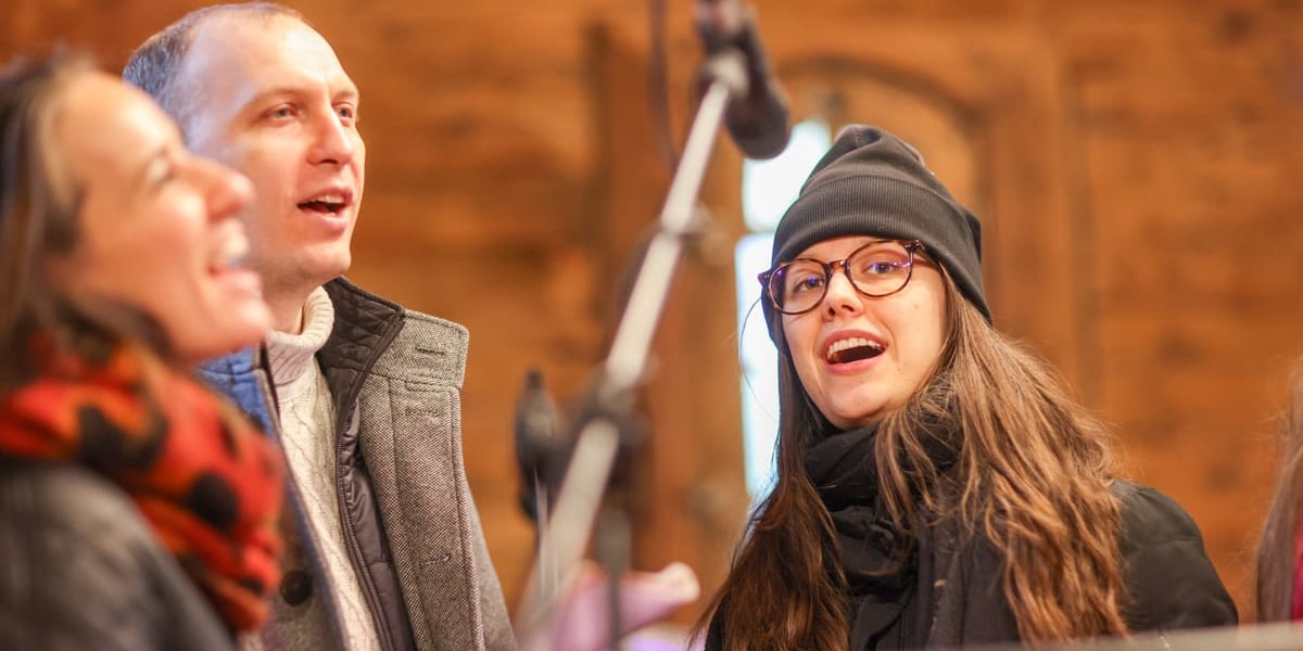 Wspólne kolędowanie w dawnym kościólku św. Jana Nepomucena, stojącym w Parku Szczytnickim. Wrocław, 24.01.2026. Na zdjęciu dwie kobiety i mężczyzna przy mirkofonie.