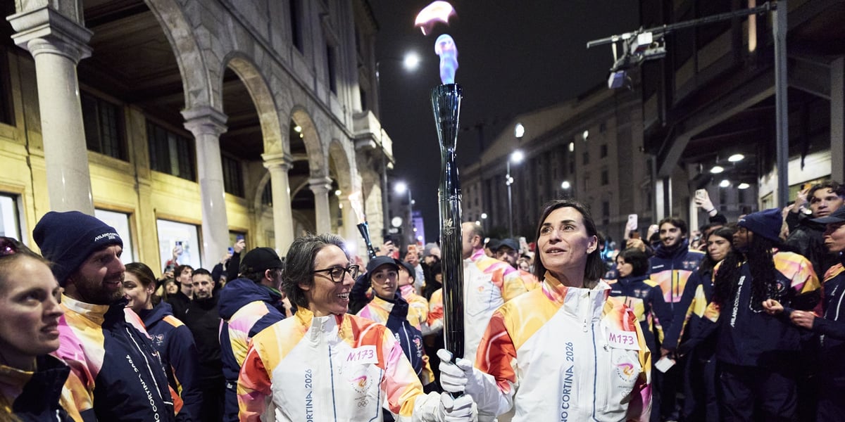 Dwie osoby niosące znicz olimpijski na ulicy w Mediolanie