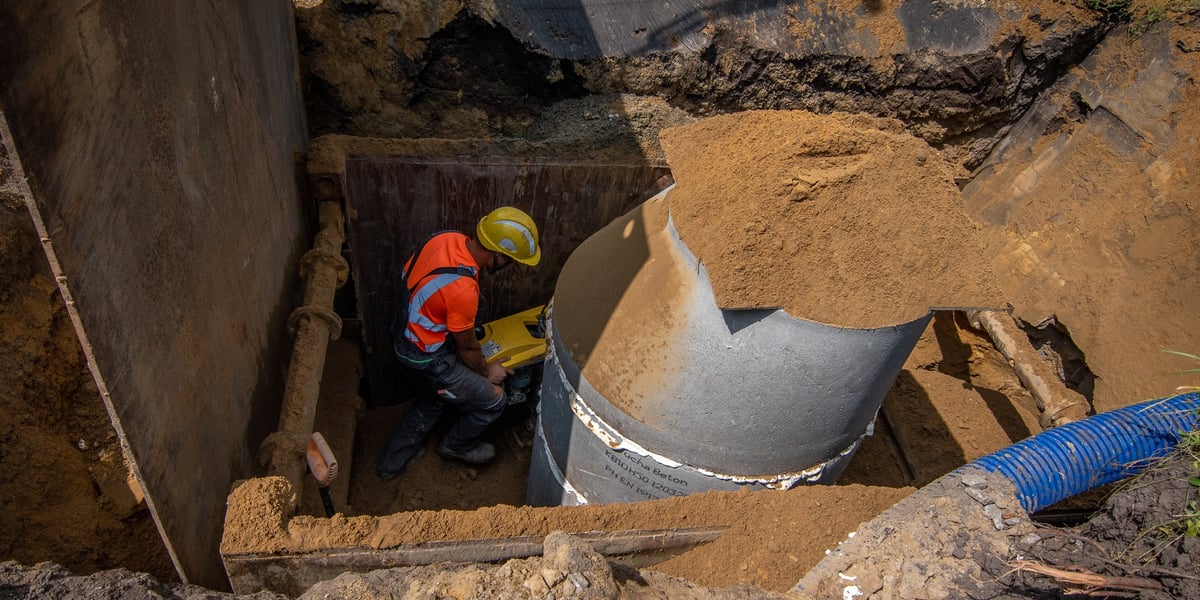 Mężczyzna w stroju roboczym montuje rurę w ziemi