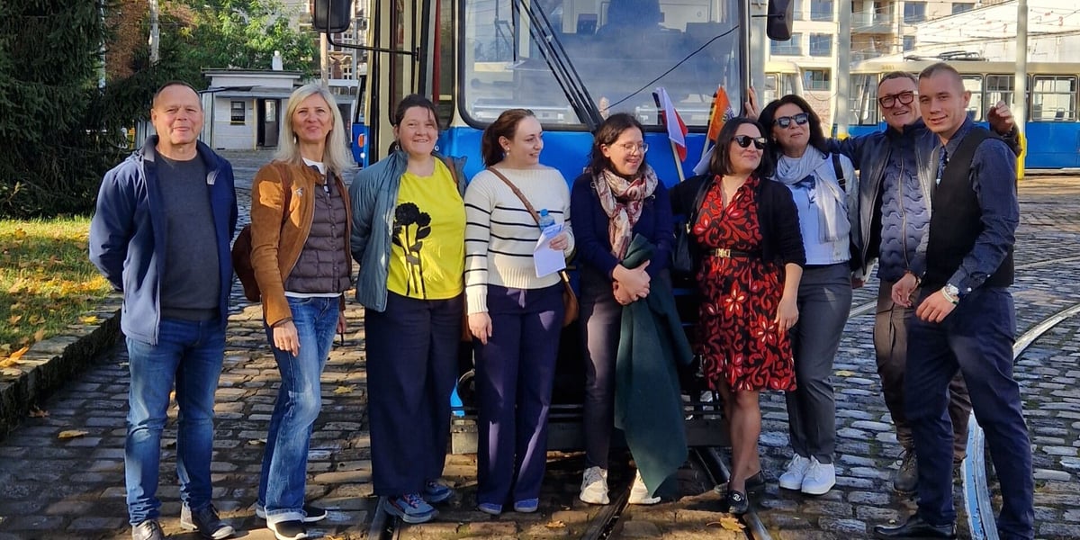Uczestnicy wizyty studyjnej we Wrocławiu, pozujący do wspólnego zdjęcia przed tramwajem w zajezdni Ołbin.