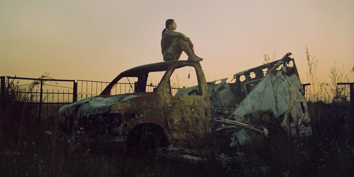 Kadr z filmu "Mariinka". Na zdjęciu kobieta w wojskowym mundurze siedzi na wraku spalonego samochodu.