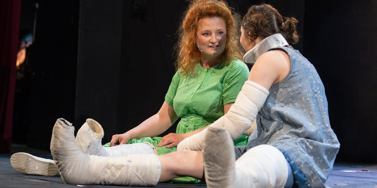 Scena ze spektaklu „Wyobraź sobie...” we Wrocławskim Teatrze Lalek – dwie aktorki z nogami w gipsie siedzą na podłodze i rozmawiają