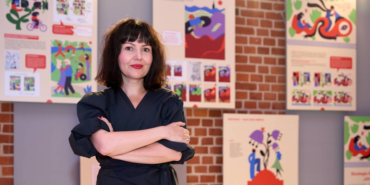 Ilustratorka Joanna Gniady na tle fragmentów „Strategii Rozwoju Wrocławia. Wrocław 2050” z grafikami jej autorstwa (wernisaż 30. Wystawy Wrocławskiej Grafiki Użytkowej)