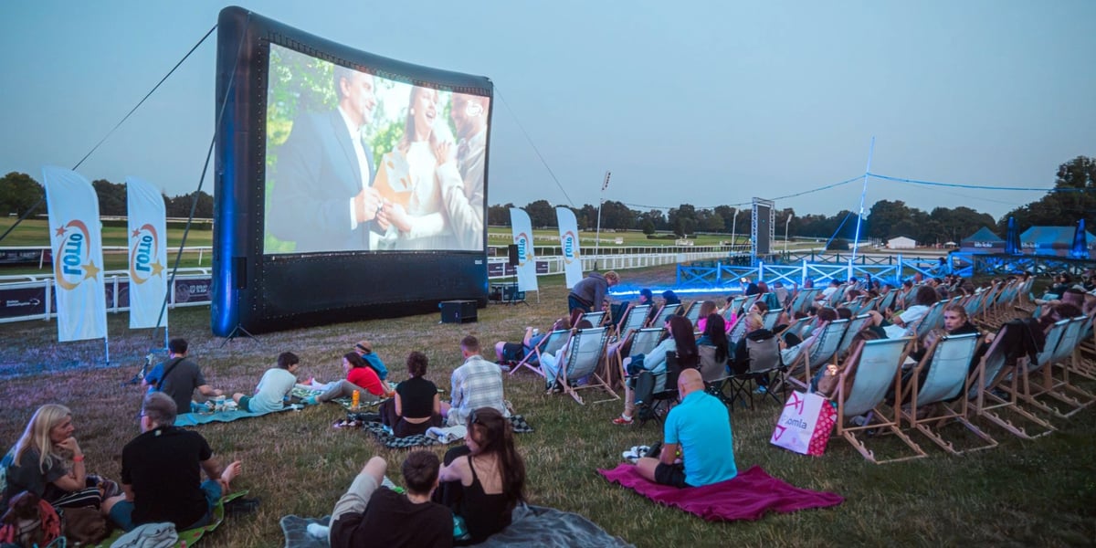 Kino plenerowe na Partynicach. Widzowie oglądają film na ekranie, który stoi tuż przy torze wyścigowym.
