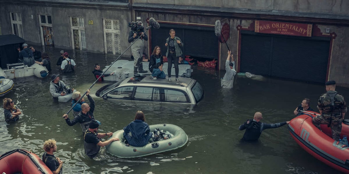 Aktorki Agnieszka Żulewska i Blanka Kot stoją na samochodzie zatopionym przez powódź, wokół pracuje ekipa filmowa. Kręcono w kąpielisku w Srebrnej Górze, gdzie odtworzono Przedmieście Oławskie 