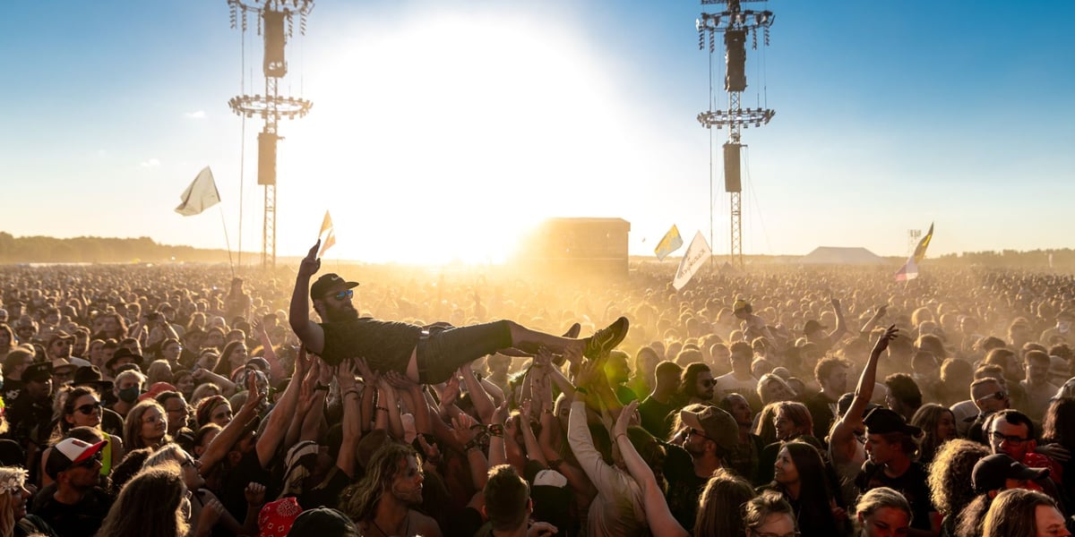 Publiczność Pol'and'Rock Festivalu niesie na rękach młodego mężczyznę w czapce z daszkiem i okularach