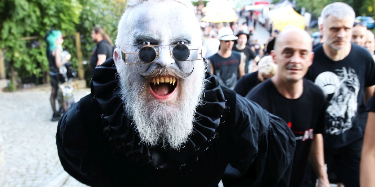 Jeden z uczestników Castle Party 2023. Mężczyzna w okularach pokazuje zęby wampira.