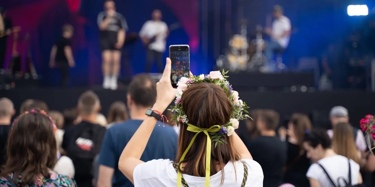 Kobieta w wianku robi smartfonem zdjęcie artystom występującym na scenie, koncert Letnie Brzmienia 2023 