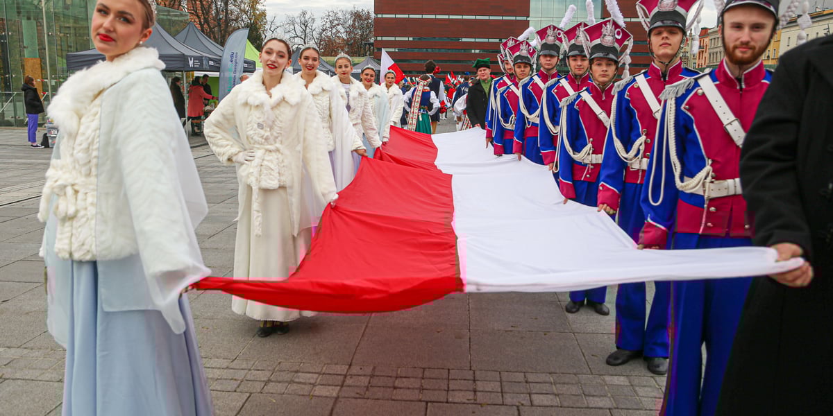 Parada Niepodległości we Wrocławiu. Zdjęcie archiwalne. Widać na nim kobiety (po lewej stronie) i mężczyzn (po prawej) ubranych w stroje historyczne, którzy trzymają polską flagę
