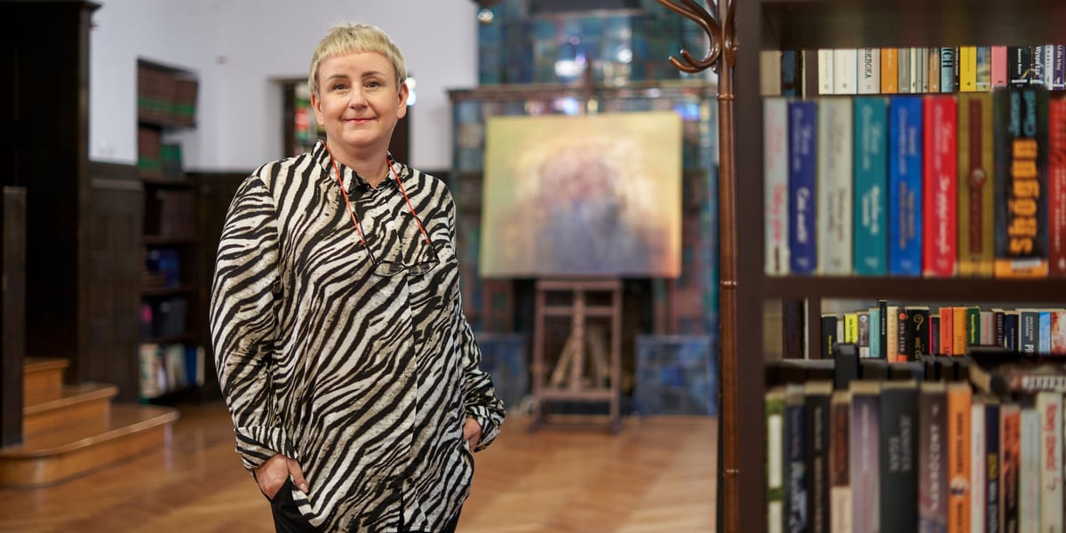 Bibliotekarka Małgorzata przy drewnianym regale z książkami