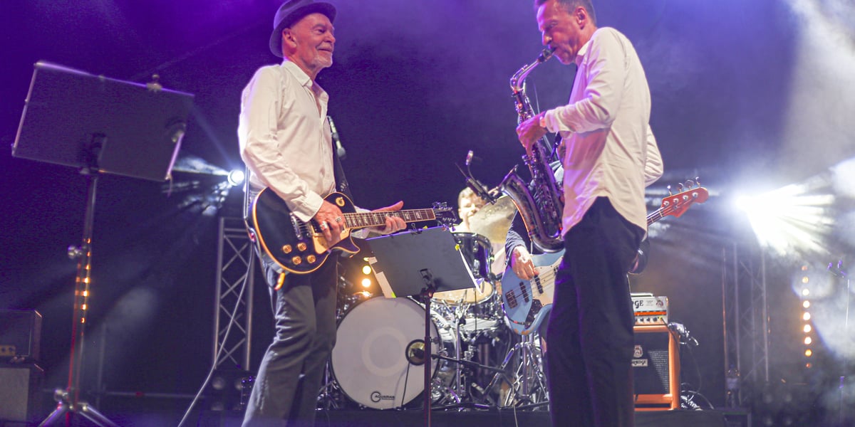 Scena oblana fioletowym światłem, dwaj mężczyźni grają na gitarach. Koncert VooVoo w Centrum Historii Zajezdnia 24.08.2024