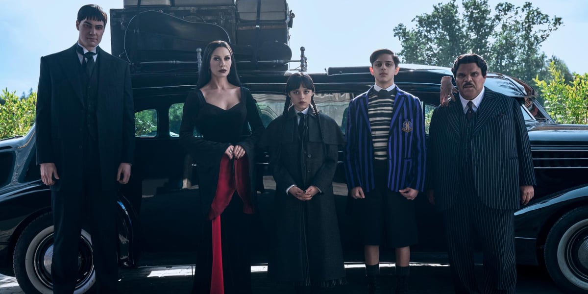 Kadr z serialu „Wednesday” Netflixa: 5 osób stoi przed czarnym samochodem, w środku Jenna Ortega (tytułowa bohaterka), obok niej z prawej Isaac Ordonez (Ajax), który będzie gościem spotkania we Wrocławiu