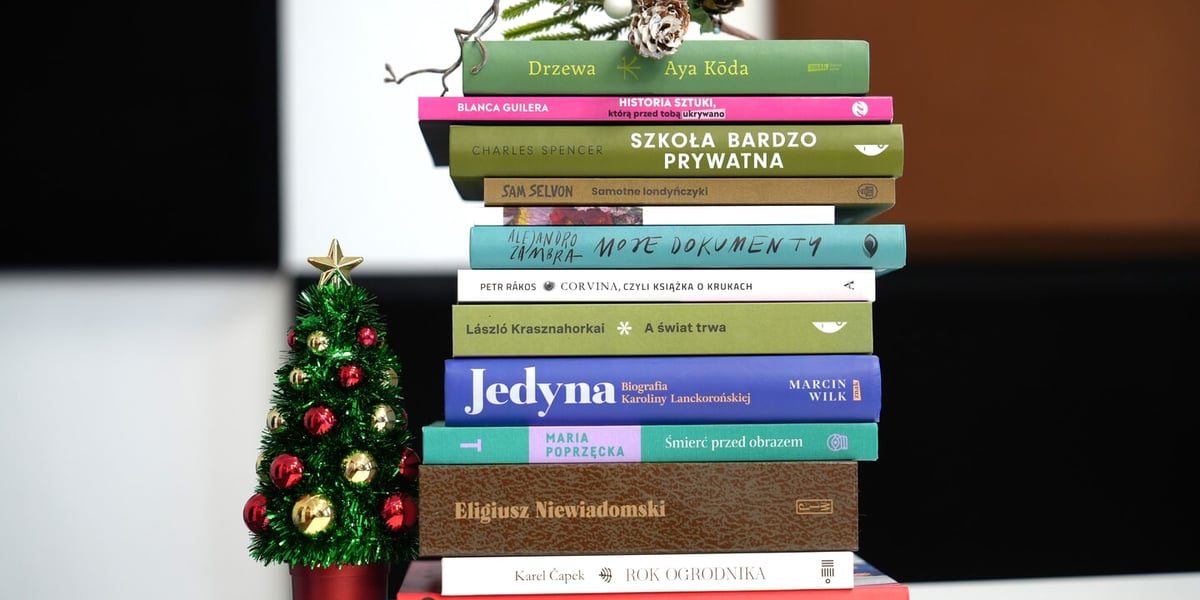 Na zdjęciu piramida z polecanych książek (odwróconych grzbietami), obok stoi choinka