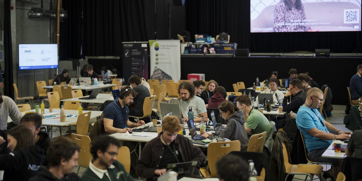 Ludzie siedzący przed komputerami, w tle duży ekran z prezentacją - CASSINI Hackathon 2026