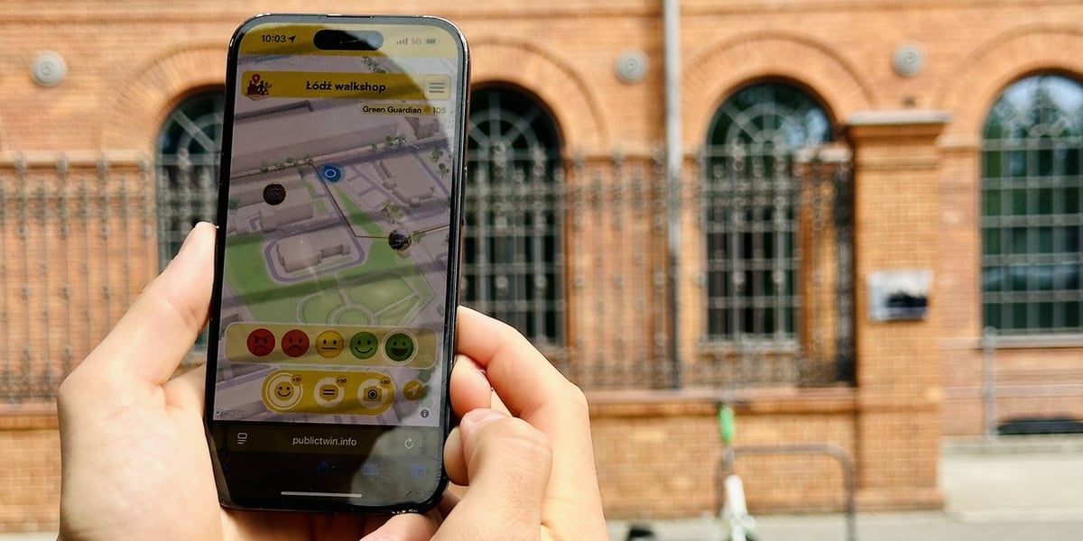 Zdjęcie przedstawia dłonie trzymające smartfon z otwartą aplikacją do oceniania przestrzeni miejskiej, na tle zabytkowego budynku z czerwonej cegły i zaparkowanej hulajnogi. Platforma PublicTwin