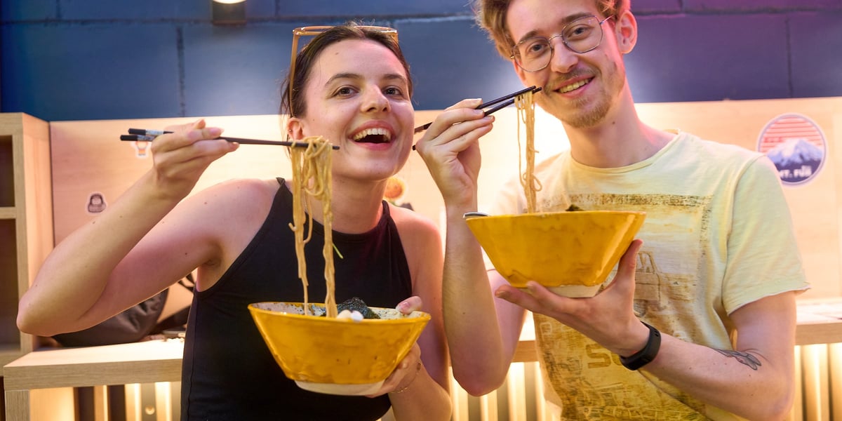 Goście Vegan AF Ramen w lokalu przy Oławskiej. Młoda, uśmiechnięta kobieta i mężczyzna z miskami ramenu.