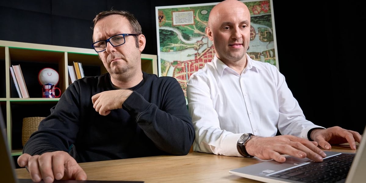 Dwóch mężczyzn siedzi przy stole, patrzą na ekrany laptopów. Od lewej strony siedzą: Bartłomiej Karaban i Łukasz Kmieć, liderzy WAIT – Wrocław AI Team. 