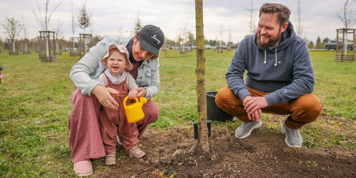 Piknik WROśnij we WROcław w powstającym parku przy ul. Rdestowej, uśmiechnięci rodzice z dzieckiem pozują przy swoim drzewku