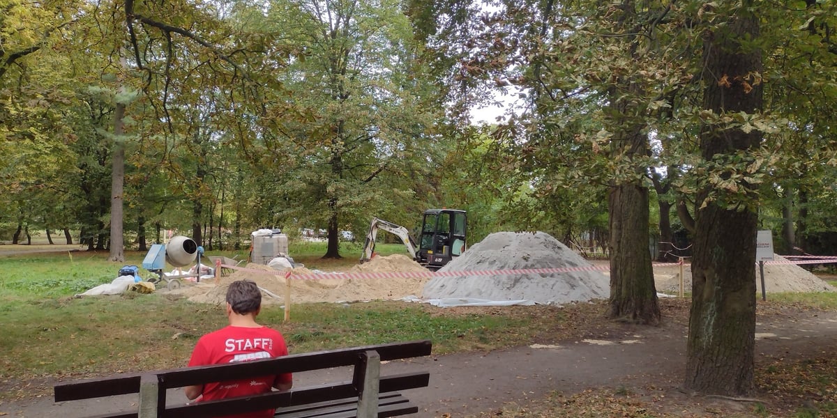 Mężczyzna siedzący na ławce w parku Skowronim, na dalszym planie: koparka