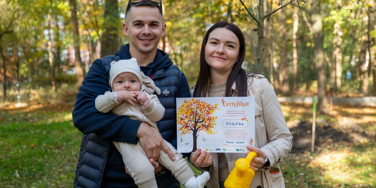 Rodzice z dzieckiem i certyfikatem zasadzenia drzewka. Uczestnicy akcji WROśnij we WROcław w parku Leśnym na Praczach 26 października.