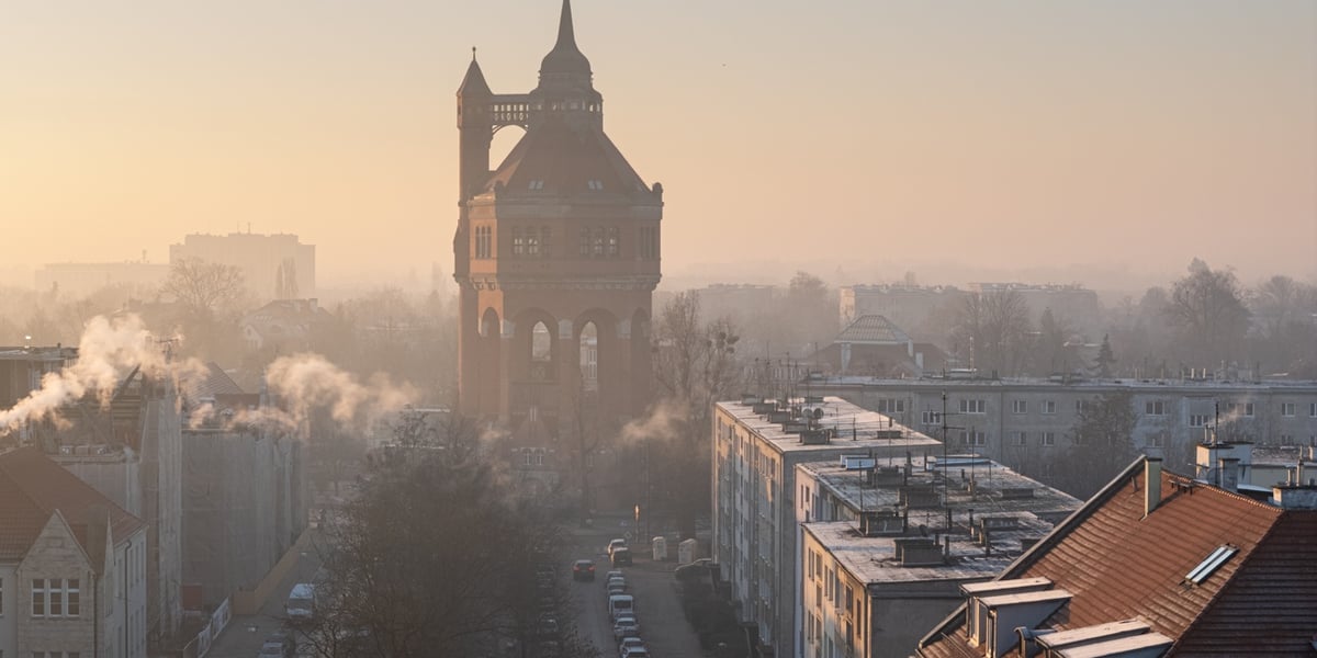 Na zdjęciu widać ulicę Sudecką, dachy budynków oraz wieżę ciśnień spowitą smogiem