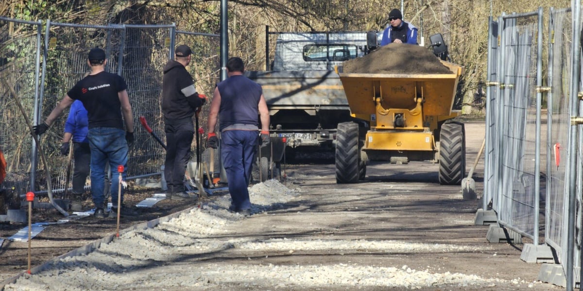 Robotnicy i maszyna budowlana wioząca ziemię na Alei Romera w Parku Grabiszyńskim.