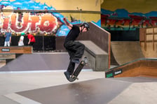 Skater w czarnym stroju i kasku wyskakuje na deskorolce w Centrum Sportów Ekstremalnych przy ul. Legnickiej 65
