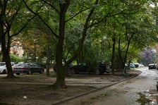 Po prawej stronie ulica podwórkowa.  Skwer i teren zieleni. Parkujące na nim samochody. W tle zabudowania mieszkalne.