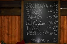 Zdjęcia z Jarmarku Bożonarodzeniowego we Wrocławiu. Na zdjęciu widać tablicę z nazwami potraw i cenami - np. żurek, flaki, grochówka - cena 23 złote