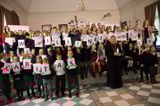 <p>Dzieci trzymające karteczki z literami mającymi układać się w napis związany ze świecami wigilijnymi Caritas</p>