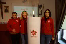 <p>Wolontariusze Caritas obok wielkiej, jubileuszowej świecy wigilijnej</p>