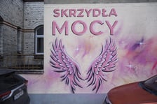 Różowe skrzydła z napisem SKRZYDŁA MOCY namalowane na ścianie szpitala na Hirszfelda