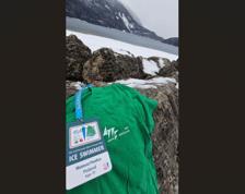 Zielona koszulka Mateusza Pawlicy i jego identyfikator z napisem Ice Swimmer na kamieniu, w tle śnieg