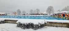 Basen na świeżym powietrzu w Malveno we Włoszech, 3-7.02.2026,  przed nim fragment żywopłotu pod śniegiem, w tle ośnieżone drzewa
