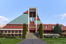 <p class="MsoNormal">Kości&oacute;ł pw. Chrystusa Kr&oacute;la budowany był w latach 1978-1991 na planie kwadratu. Budowla przypomina ostrosłup złożony z czterech części, podobnych do wież, o zr&oacute;żnicowanej wysokości. Zbiegające się <span style="mso-spacerun: yes;">&nbsp;</span>ku środkowi ściany owych wież przykrywają centralną (sakralną) część budowli, nadając jej ekspresyjny charakter. Nachylone połacie zdobi dekoracja przypominająca strukturę kryształu. W przyziemiu mieści się kaplica św. Mikołaja, ośrodek kultury i szkoła.</p>