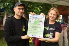 <p>Kobieta i mężczyzna trzymający plakat z zaproszeniem na piknik Ekosystemu</p>