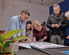 Przykład spotkania konsultacyjnego. Dyskutujący uczestnicy pochyleni nad koncepcją zagospodarowania podwórka.