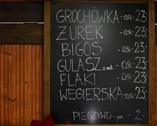 Zdjęcia z Jarmarku Bożonarodzeniowego we Wrocławiu. Na zdjęciu widać tablicę z nazwami potraw i cenami - np. żurek, flaki, grochówka - cena 23 złote
