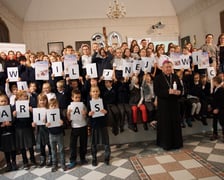 <p>Dzieci trzymające karteczki z literami mającymi układać się w napis związany ze świecami wigilijnymi Caritas</p>