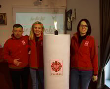 <p>Wolontariusze Caritas obok wielkiej, jubileuszowej świecy wigilijnej</p>