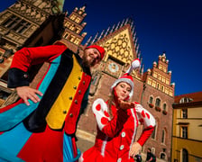 Dwoje szczudlarzy w barwnych, bajkowych strojach krasnali pozuje na tle zabytkowego Starego Ratusza we Wrocławiu