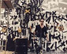 Krzysztof Cichoń na tle swojego muralu w podwórku neonów przy ulicy Ruskiej we Wrocławiu