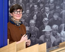 <p>Agata Gabiś, jedna z kuratorek wystawy "Niedziela w Hutmenie" w Muzeum Architektury we Wrocławiu, w tle zdjęcie pracownik&oacute;w zakładu ze zbior&oacute;w Ossolineum wykonane przez S. Kokurewicza w 1975 roku</p>