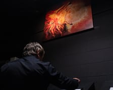 <p>Z wizytą w Niewidzialnym Domu we Wrocławiu. Na zdjęciu mężczyzna w ciemnym pomieszczeniu. Ponad jego głową, na ścianie wisi obraz.&nbsp;</p>