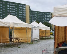 Puste stanowiska handlowe. Białe namioty. W tle zabudowania osiedla i duże bloki.