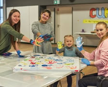 Warsztaty plastyczne w prowadzonym przez Fundację Ukraina Centrum Ukraińskiej Kultury i Rozwoju (CUKR). Na zdjęciu trzy kobiety i mała dziewczynka tworzące obraz przy pomocy zanurzanych w farbie dłoni.