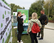 Trójka ludzi stoi w parku obok wózka konsultacyjnego i rozmawia.