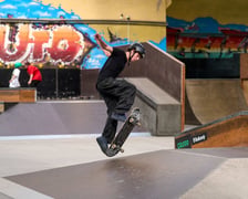 Skater w czarnym stroju i kasku wyskakuje na deskorolce w Centrum Sportów Ekstremalnych przy ul. Legnickiej 65
