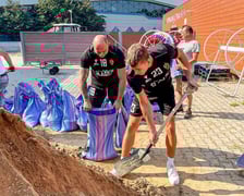 Piłkarze ręczni Śląska (ubrani w klubowe stroje) nasypują łopatami piach do worków i wrzucają je na naczepę
