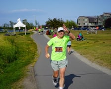 Maratończyk, senior prof. Jan Chmura biegnący ostatnie 20 km w maratonie na Alasce. W tle widać innych zawodników, kibiców i domy